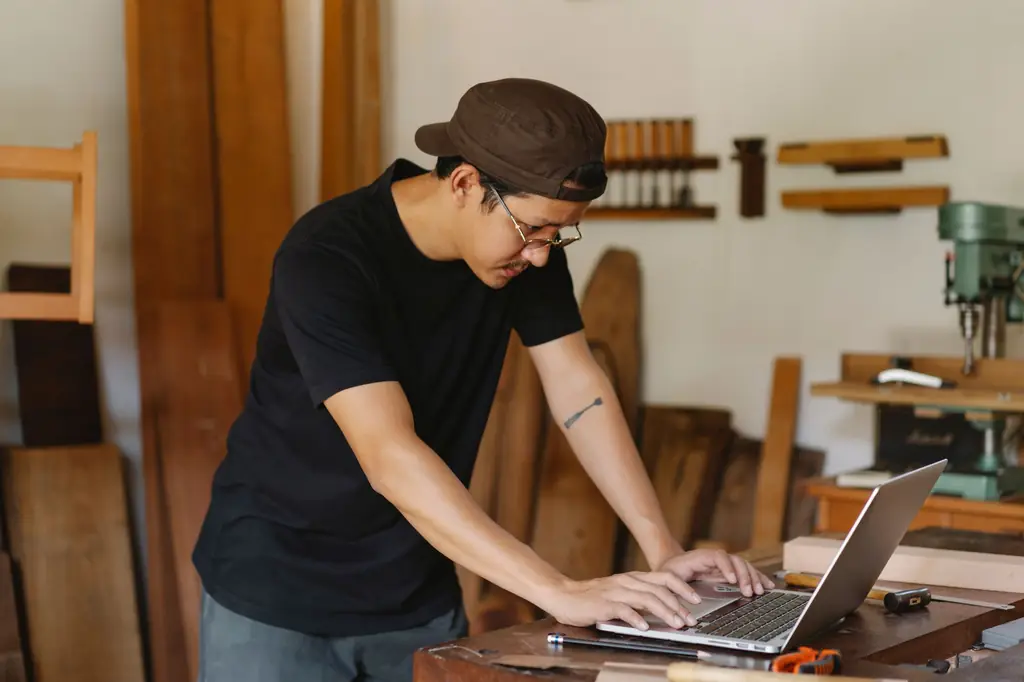 A craftsman working on a laptop in his woodworking shop