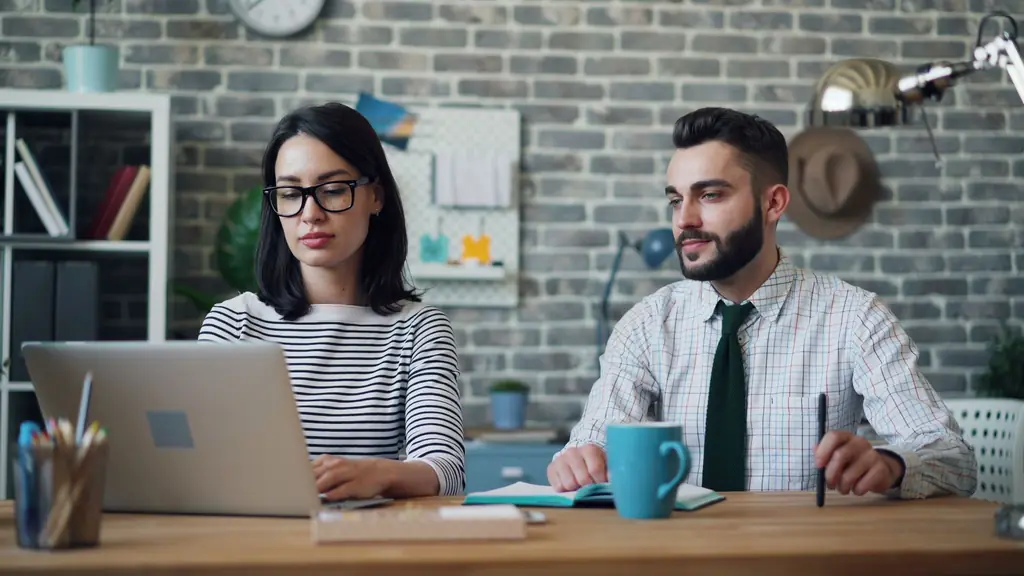 Two colleagues reviewing work together on a laptop at a shared desk