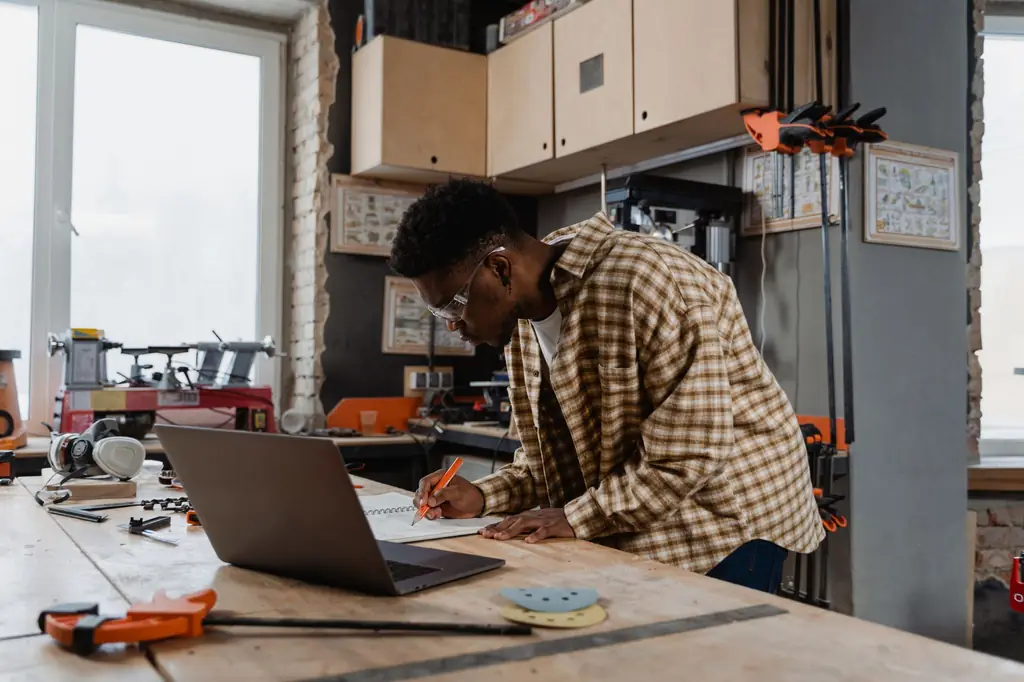 A shop owner planning work on a laptop at his workbench
